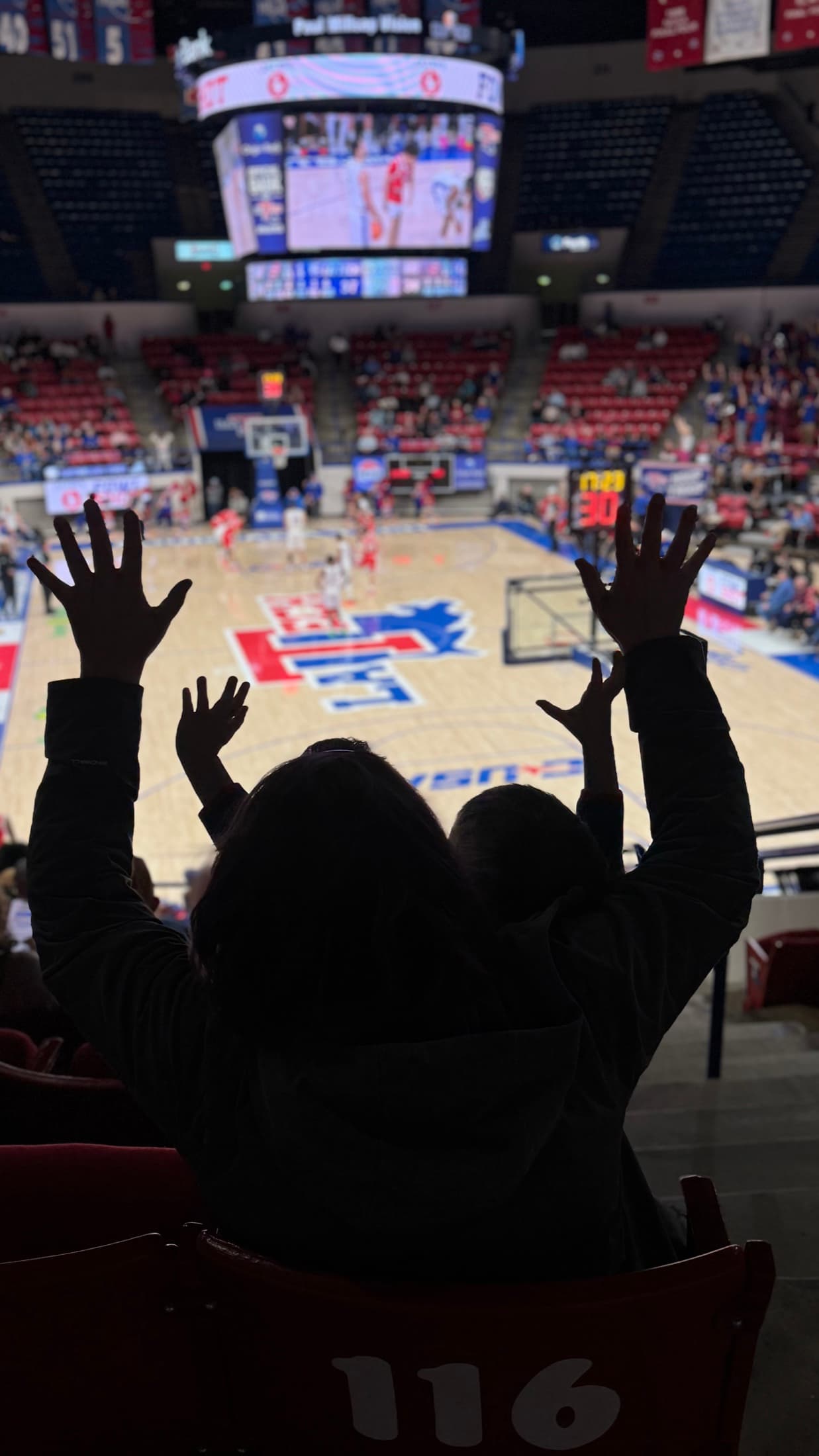 Two young fans raise their hands while watching a Louisiana Tech basketball game from the stands